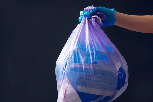 Χέρι στο ιατρικό γάντι ρίχνουν σακούλες σκουπιδιών. Η χρησιμοποιημένη μάσκα προσώπου. — Φωτογραφία Αρχείου