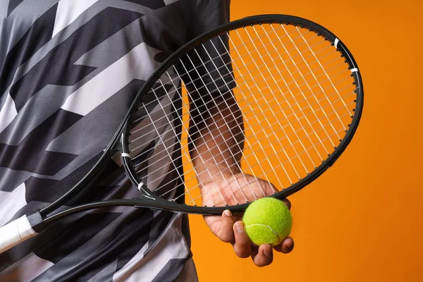 Primer plano de un jugador de tenis mano con raqueta y pelota contra fondo naranja — Foto de Stock