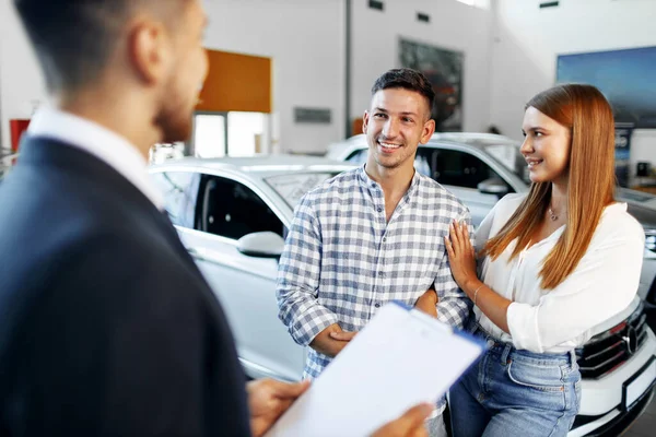 Autoverkäufer erzählt dem Paar von den Eigenschaften des neuen Autos — Stockfoto