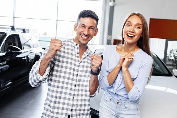 Cherrful jovem casal na concessionária comprar um carro novo — Fotografia de Stock