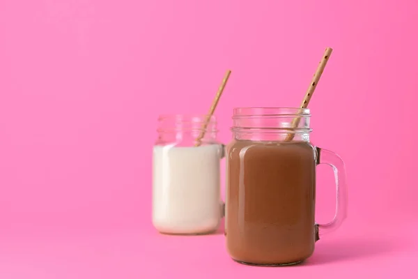 Pots en verre avec milkshakes aromatisés sur fond rose — Photo