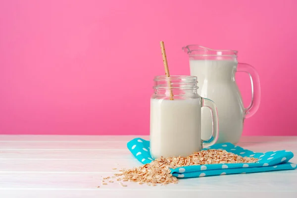 Leche de avena en cristalería y copos de avena secos sobre fondo rosa — Foto de Stock