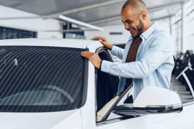 Yeni arabasında oturan yakışıklı, mutlu, Afro-Amerikan bir adamın portresi.