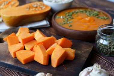 Masadaki tahta tahtada çiğ balkabağı parçaları kes.