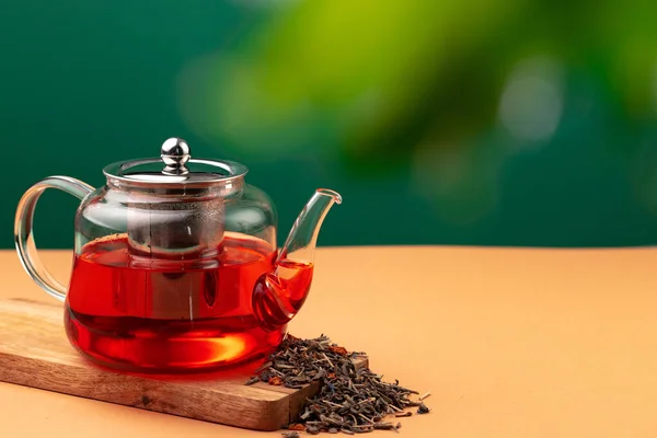 Théière en verre avec thé noir sur fond de feuillage flou — Photo