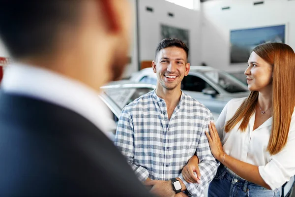 Homem vendedor de carros contando sobre as características do carro novo para o casal — Fotografia de Stock