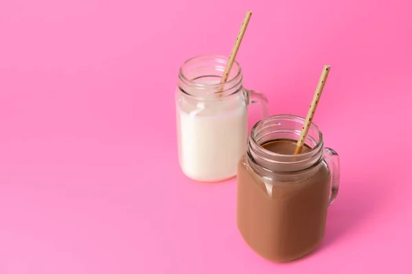 Glass jars with flavoured milkshakes against pink background — Stock Photo, Image