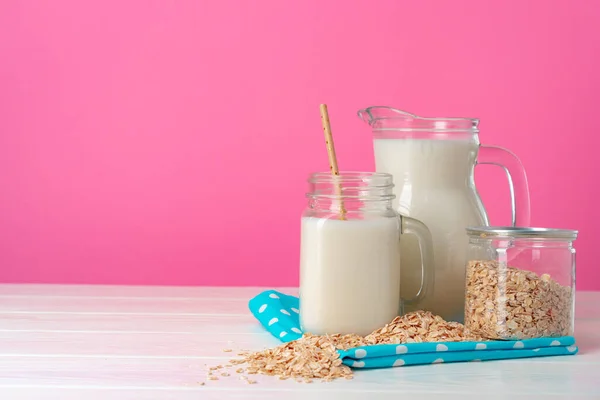 Вівсяне молоко в скляному посуді і сухі вівсяні пластівці на рожевому фоні — стокове фото