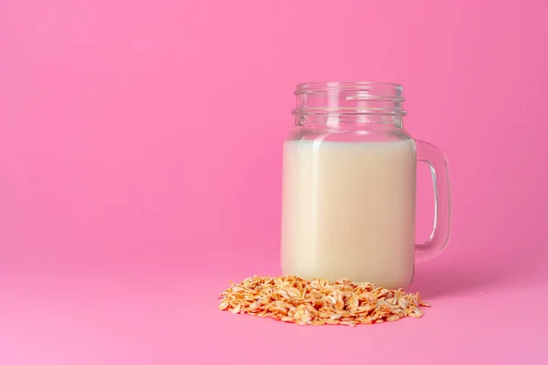 Oat milk in glassware and dry oat flakes on pink background — Stock Photo, Image