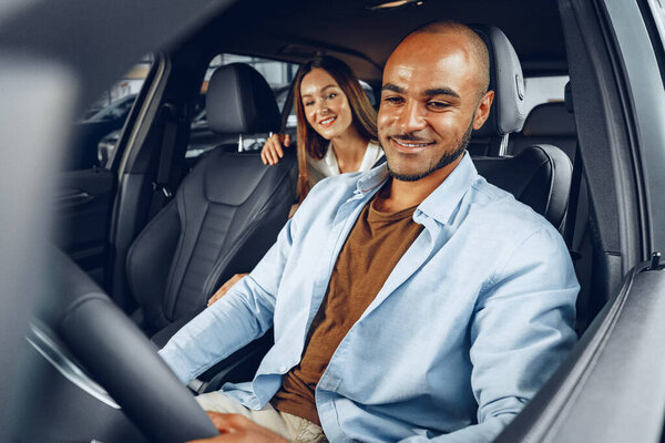 Молодая привлекательная женщина продавец в автосалоне показывает машину своему клиенту