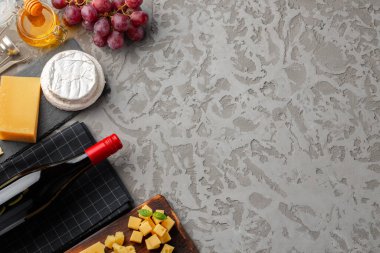 Gri arka planda şarap şişesi ve peynir çeşitleriyle kompozisyon