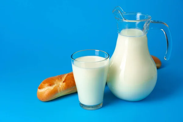 Свежий багет и кувшин со свежим молоком на синем фоне — стоковое фото