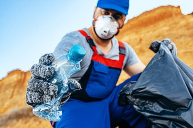 Plajı temizleyen bir çöp torbasına plastik çöp atan gönüllü bir adam.