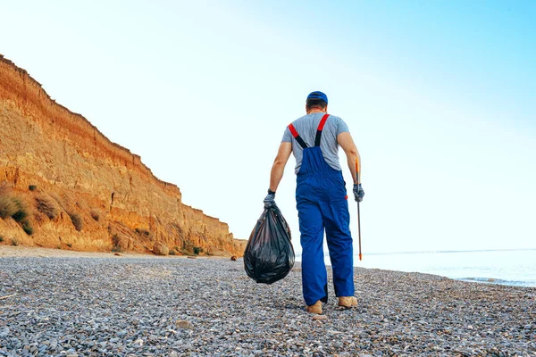 Férfi önkéntes gyűjtése szemetet a strandon egy elérési meghosszabbító bottal — Stock Fotó