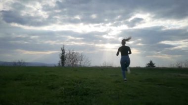 Gün batımında, koşu genç kadın hava, gençlik ve mutluluk, Beautiful bulutlar ve nefes kesen günbatımı silah yükseltir. Steadicam ağır çekim video