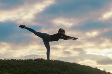 Genç kadının tek ayak üstünde duran ve üzerinde çim sabah egzersiz