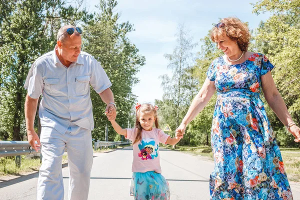 family, generation and people concept - happy smiling grandmother, grandfather and little granddaughter walking at park