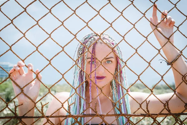 sexy girl in a swimsuit with pigtails with sunglasses standing near a metal grate fence, portrait, bit her lip