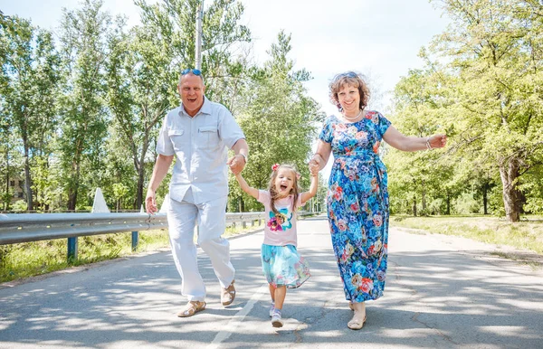 Familj, generation och människor koncept - glada leende farmor, farfar och lilla barnbarn promenader på park Stockbild