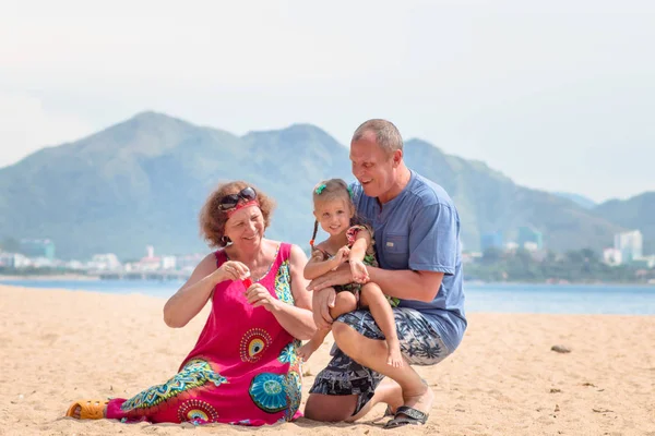 Farföräldrar njuta av dagen med barnbarn medan blåser såpbubblor på stranden nära havet Stockfoto