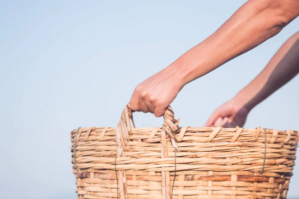 strong male hands hold a wicker basket on the background of the sea