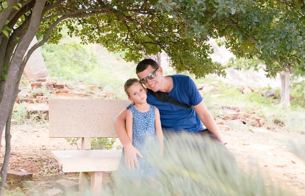 Père et petite fille jouissent d'une vue dans un parc arboré, assis sur un banc. Enfants et papa ensemble . — Photo