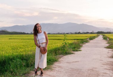 Yol kenarında yürüyen bir kadın çantasıyla turist gibi yürüyor.