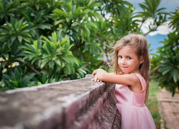 Ritratto di una bambina felice in abito rosa all'aperto, vicino al muro Immagine Stock