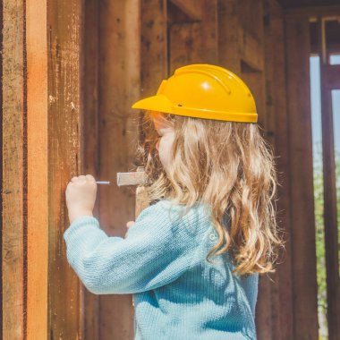 bir çocuk, bir çekiç ile bir ahşap çerçeve ev inşaat alanında bir kask bir kız ve onun elinde çivi