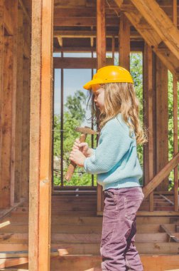 bir çocuk, bir çekiç ile bir ahşap çerçeve ev inşaat alanında bir kask bir kız ve onun elinde çivi