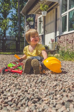 Çocuk, kız Oluşturucu kask ve oyuncak araç seti ile açık havada evin taş üzerinde oturur