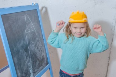 Çocuk mühendis, tasarımcı, kız bir kask boya siyah tebeşir tahtası üzerinde bir evde