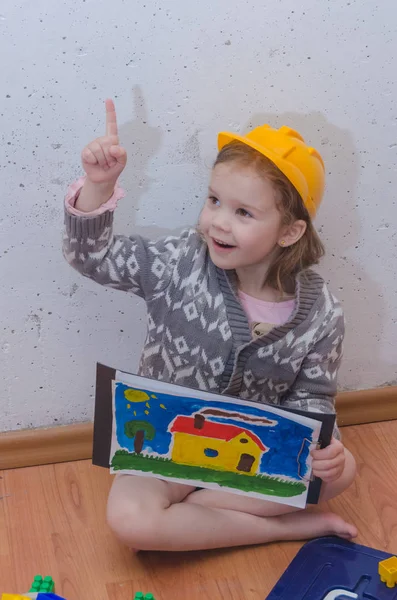 室内的孩子 一个女孩在一个头盔的建设者收集设计师 房子根据图纸 — 图库照片