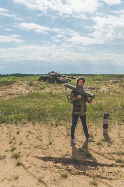 Güneşli bir gün kız kırık bir tank savaş alanında arka plan üzerinde bazukayla üniformalı