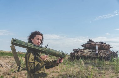 Güneşli bir gün kız kırık bir tank savaş alanında arka plan üzerinde bazukayla üniformalı