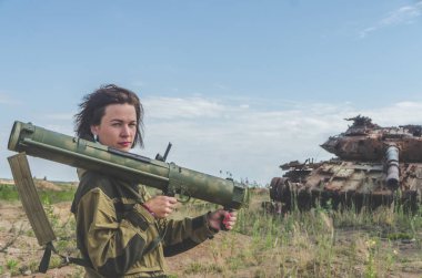 Güneşli bir gün kız kırık bir tank savaş alanında arka plan üzerinde bazukayla üniformalı