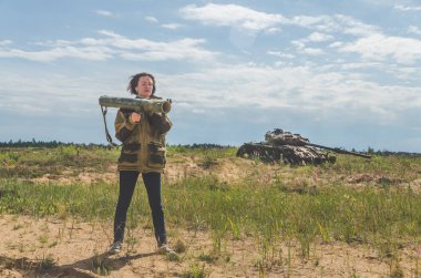 Güneşli bir gün kız kırık bir tank savaş alanında arka plan üzerinde bazukayla üniformalı