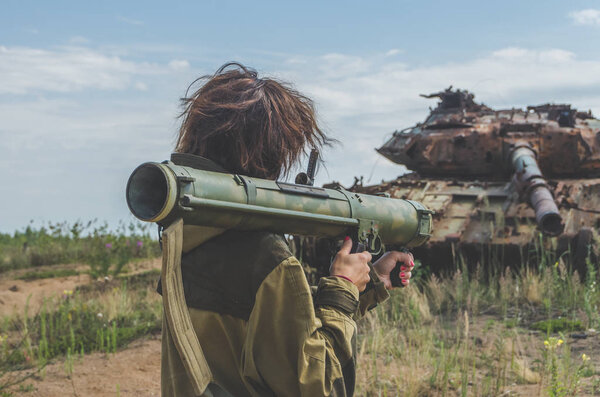 Sunny day girl in uniform with a Bazooka on the background of a broken tank on the battlefield