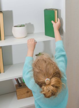 Kız, çocuk kitabı rafa koyar