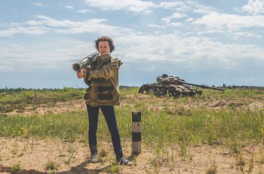 elleri yok şekildepaslı savaş alanında arka plan üzerinde de bir bazuka ile askeri üniforma ve kot pantolon güzel kız