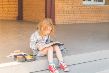 Güneşli bir gün okulda bir kız, bir çocuk dışında bir kitap ile öğle yemeğinde kırmak