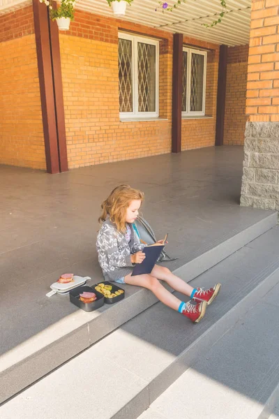 on a Sunny day at school break a girl, a child outside, at lunch with a book