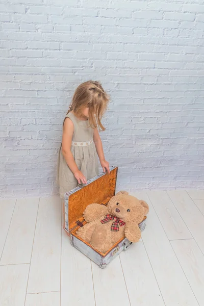 Kız, bebek elbise bavul, oyuncak ayı ile beyaz tuğla duvar zemin üzerine