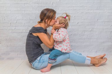 Kız, anne ve çocuk Patty-kek ve öpücük oynayan bir beyaz tuğla duvar önünde