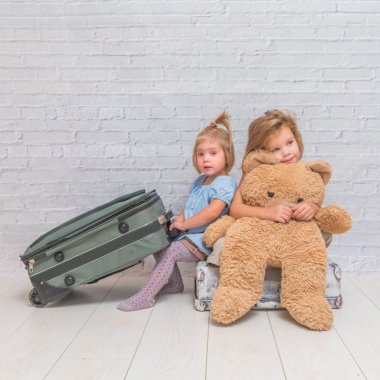 iki kız, beyaz tuğla tekerlekli bavula çocuklarla arka plan duvar.