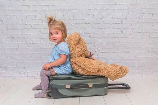 在白色砖墙背景下的孩子坐在一个手提箱 他的背部转向玩具熊 — 图库照片