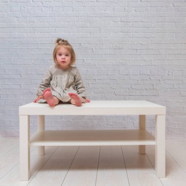 Kız, beyaz duvara karşı masa üstünde oturan çocuk