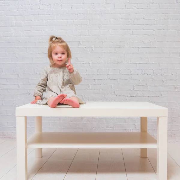 Kız Beyaz Duvara Karşı Masa Üstünde Oturan Çocuk — Stok fotoğraf