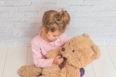 kız çocuk beyaz duvara karşı bir oyuncak ayının sıcaklık ölçer