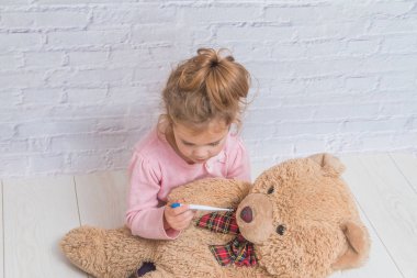 kız çocuk beyaz duvara karşı bir oyuncak ayının sıcaklık ölçer